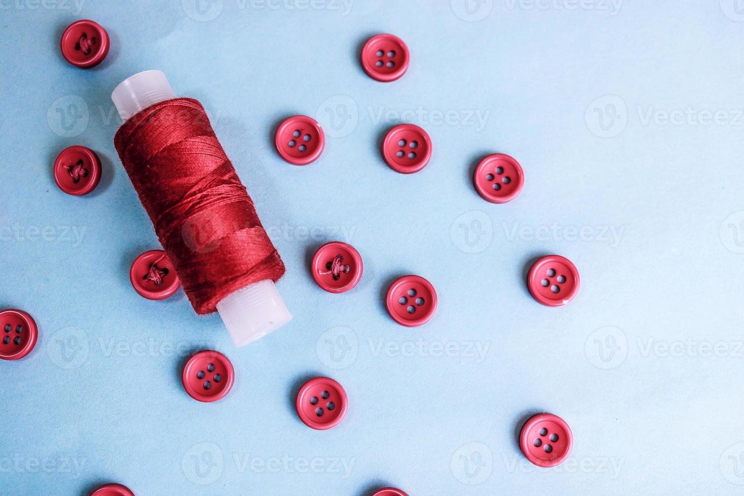 Beautiful texture with lots of round red buttons for sewing, needlework and a coil of thread. Copy space. Flat lay. Blue background photo