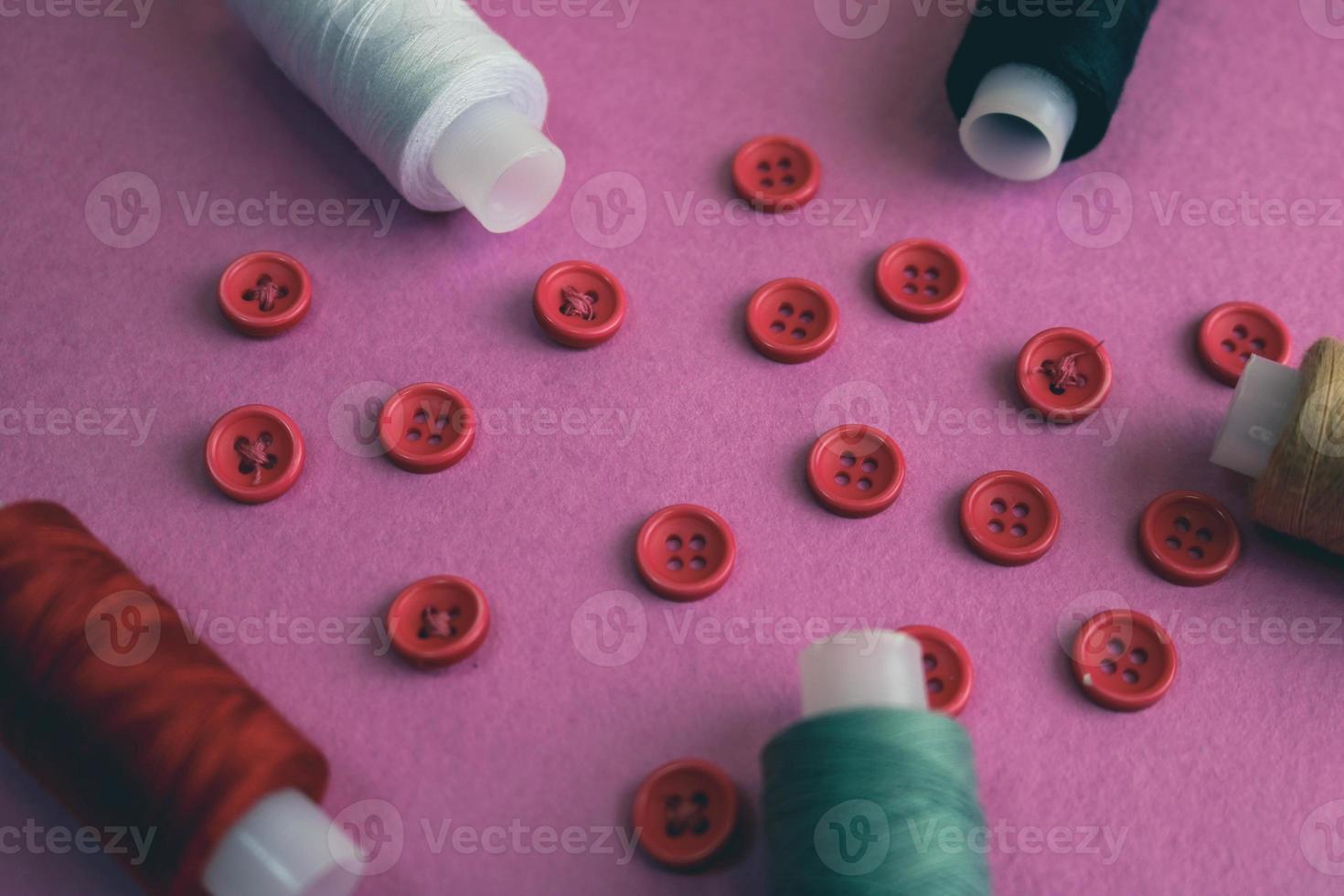 Beautiful frame with a lot of round red buttons for sewing, needlework and skeins of spools of thread. Copy space. Flat lay. Purple pink background photo
