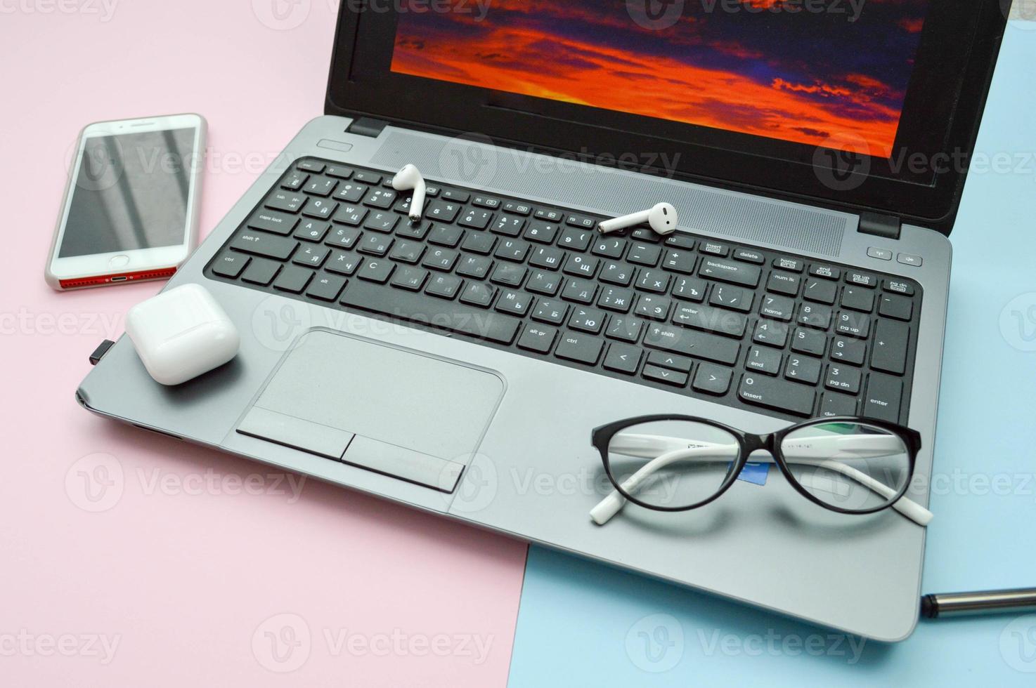 Workplace at home, home office for remote work with a computer laptop mobile phone smartphone notepad pen headphones and glasses on a pink and blue background photo