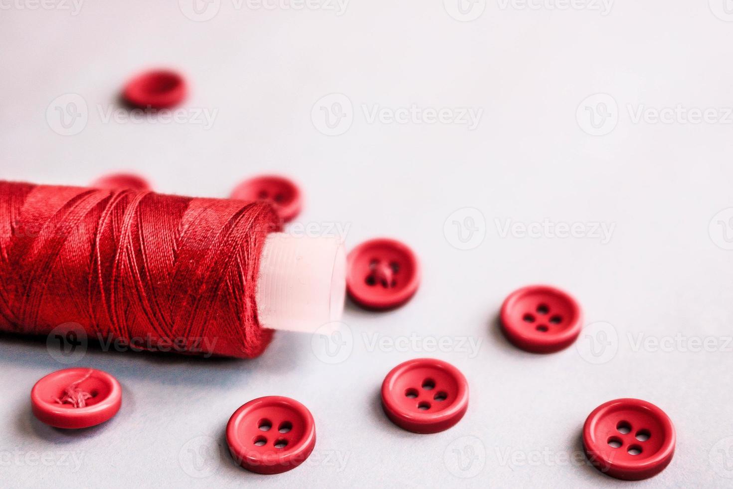 Beautiful texture with lots of round red buttons for sewing, needlework and a coil of thread. Copy space. Flat lay. White background photo
