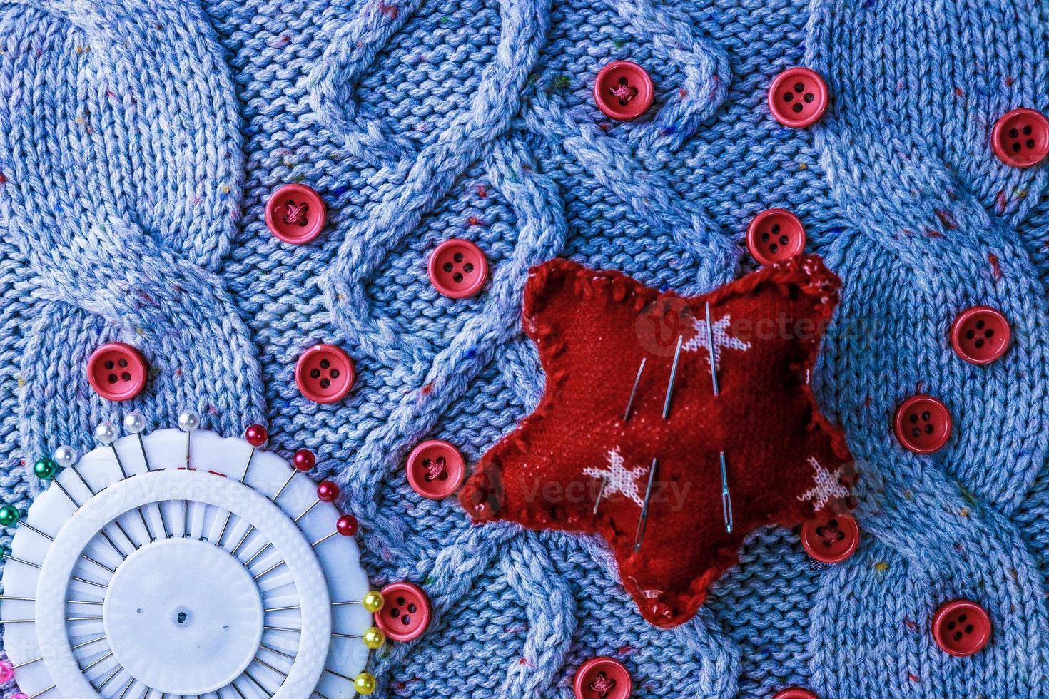 Beautiful texture of a soft warm natural sweater, knitted fabrics and red small round buttons for sewing and a needle pad. Flat lay. The background photo