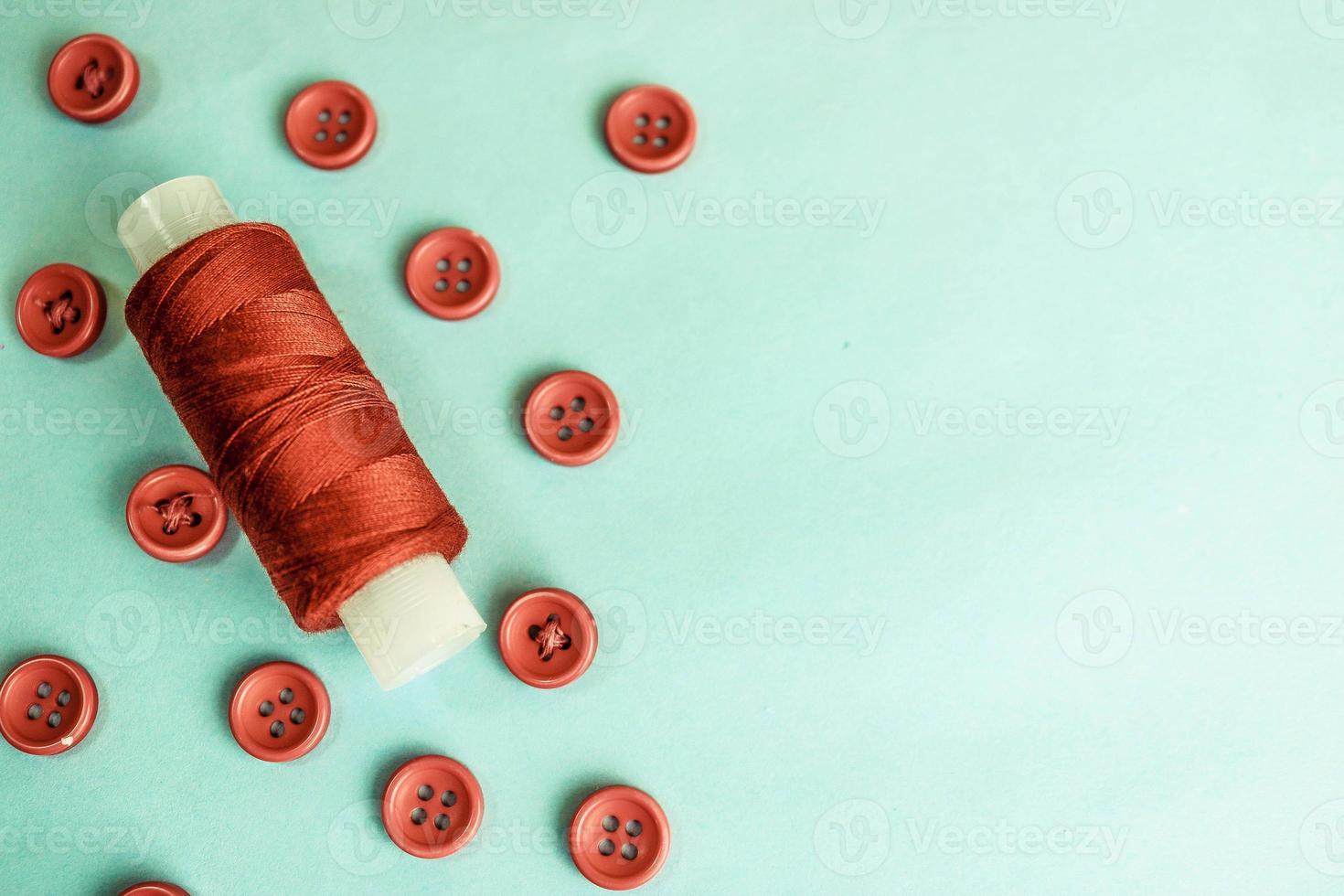 Beautiful texture with lots of round red buttons for sewing, needlework and a coil of thread. Copy space. Flat lay. Blue background photo