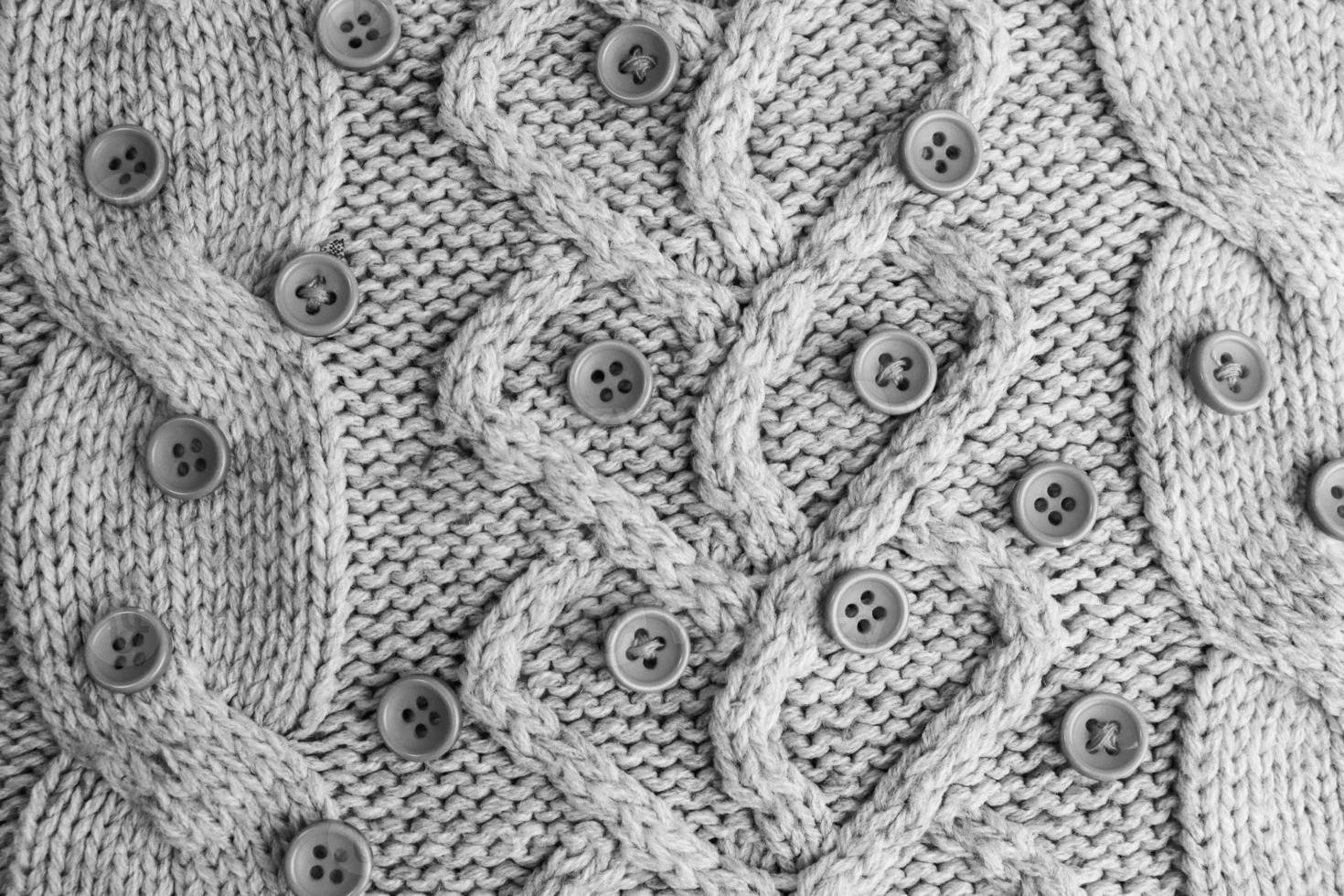 Beautiful texture of a soft warm natural sweater with a knitted pattern of yarn and black and white small round buttons. The background photo