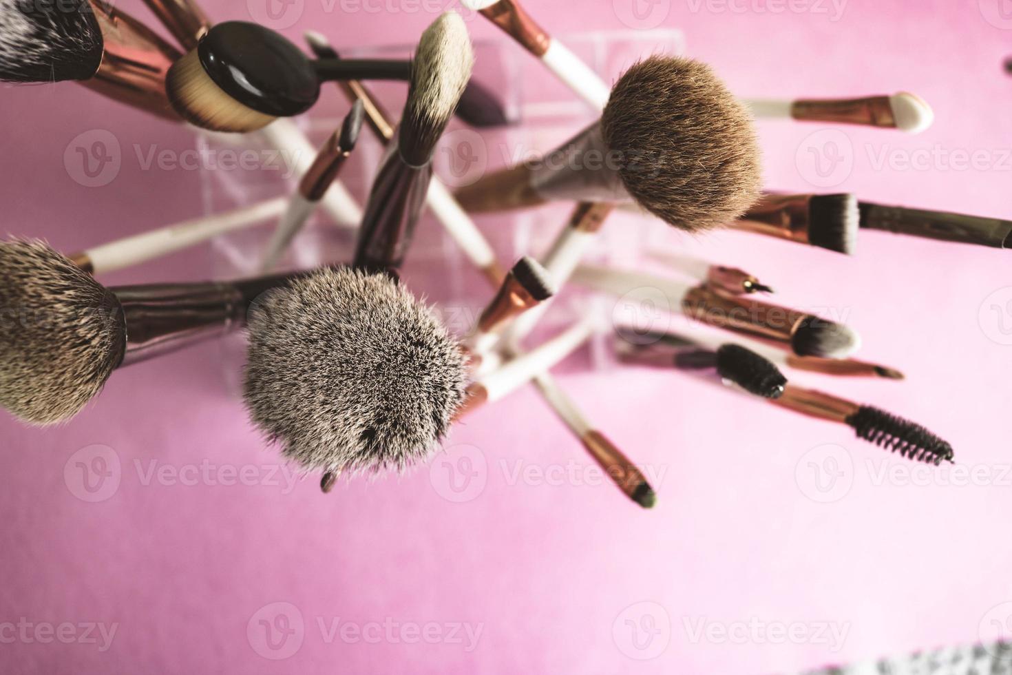 un conjunto de hermosos pinceles suaves diferentes para el maquillaje de la siesta natural para la orientación de la belleza y la aplicación de una base tonal en un espacio de soporte y copia sobre un fondo rosa y púrpura foto