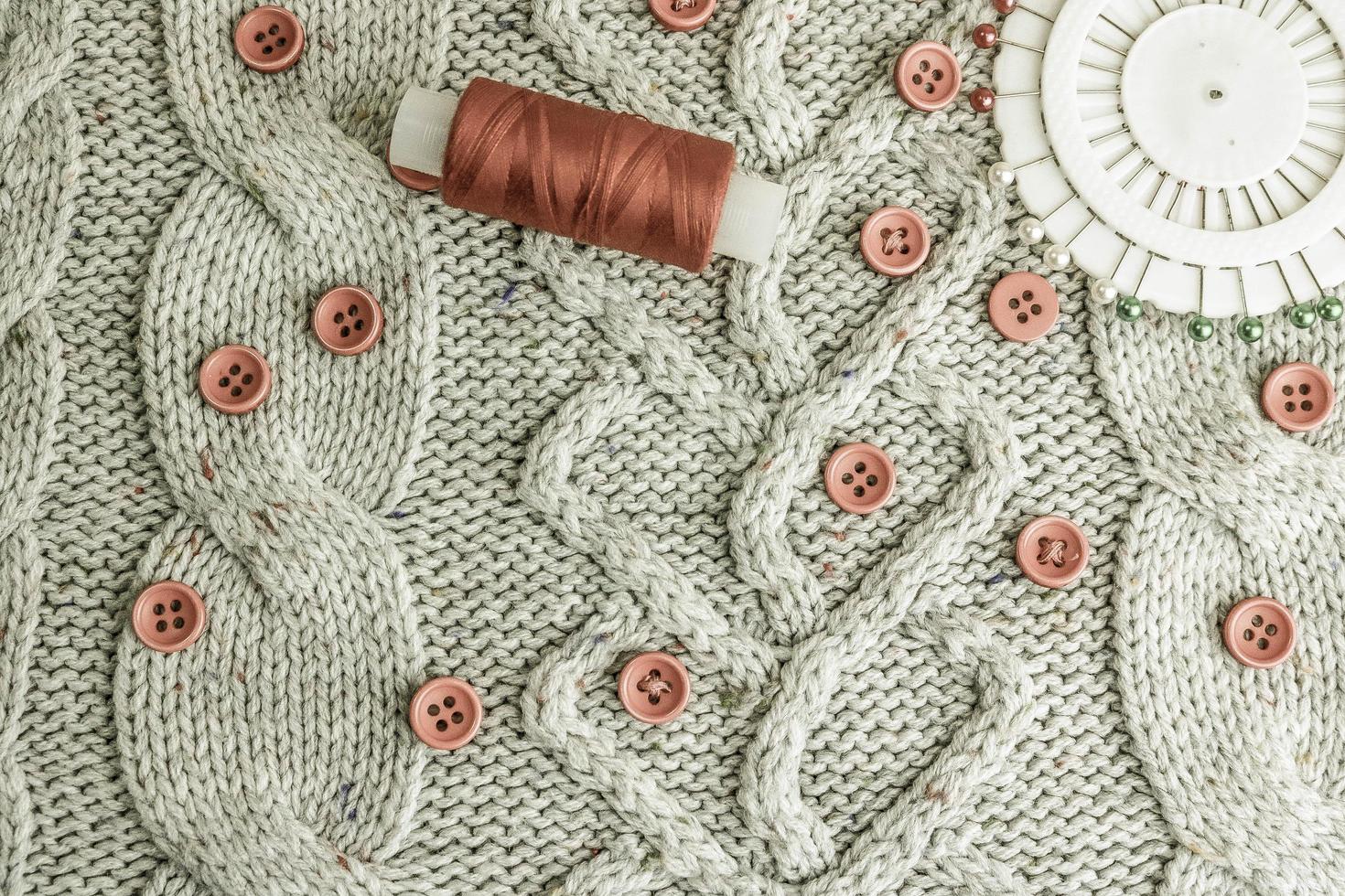 Beautiful texture of a soft warm natural sweater, knitted fabrics and red small round buttons for sewing and a skein of thread, needle bed. Flat lay. The background photo