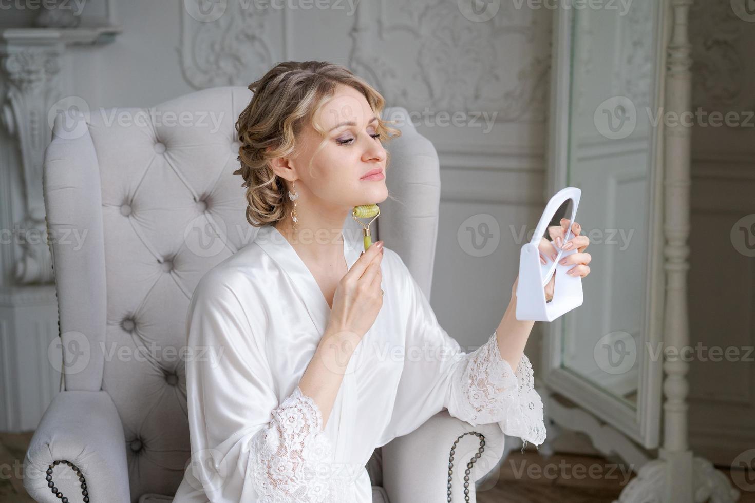 Roller face. Woman in silk robe makes facial massage. Lady in elegant home photo