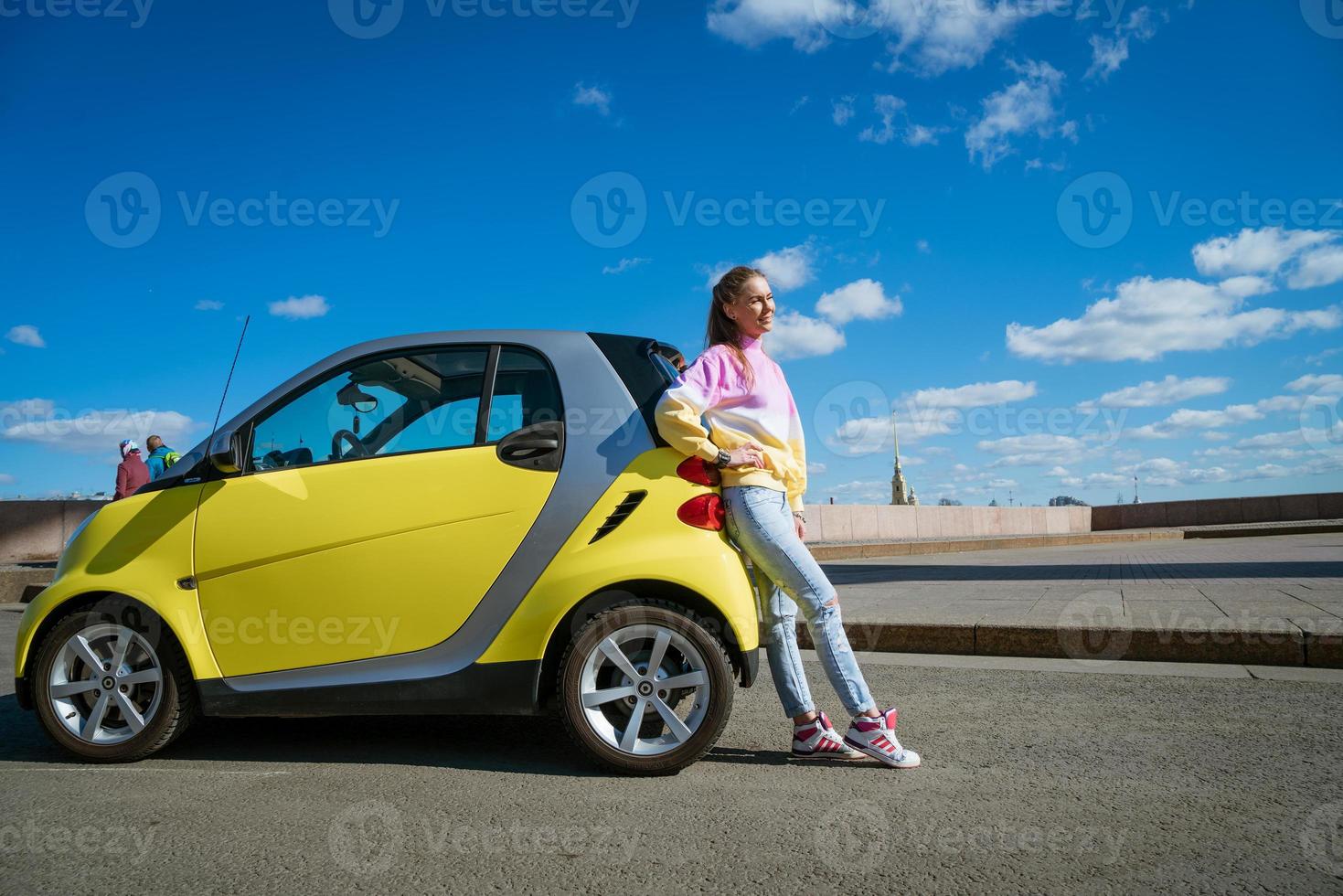 12.04.2019 Russia Saint Petersburg. A young happy woman stands by a smart fortwo car against a blue sky with clouds photo