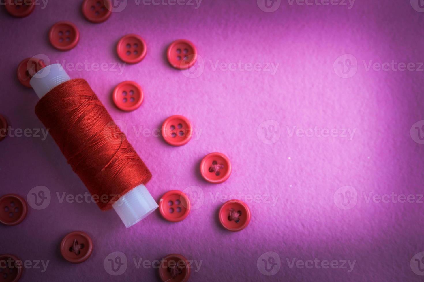 Beautiful texture with many round pink buttons for sewing, needlework and a coil of thread. Copy space. Flat lay. Pink, purple background photo