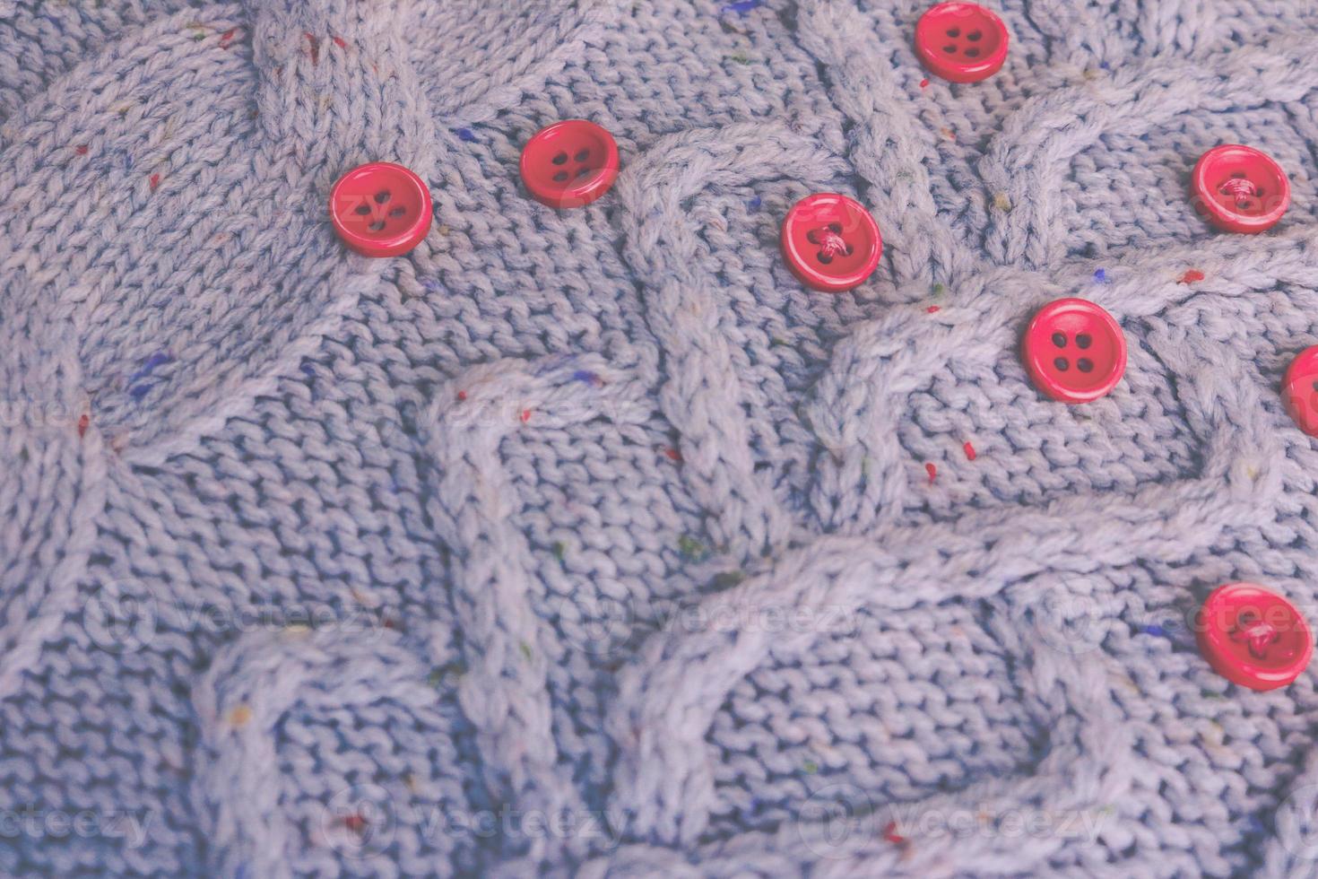 Beautiful texture of a soft warm natural sweater with a knitted pattern of yarn and red small round buttons for sewing. The background photo