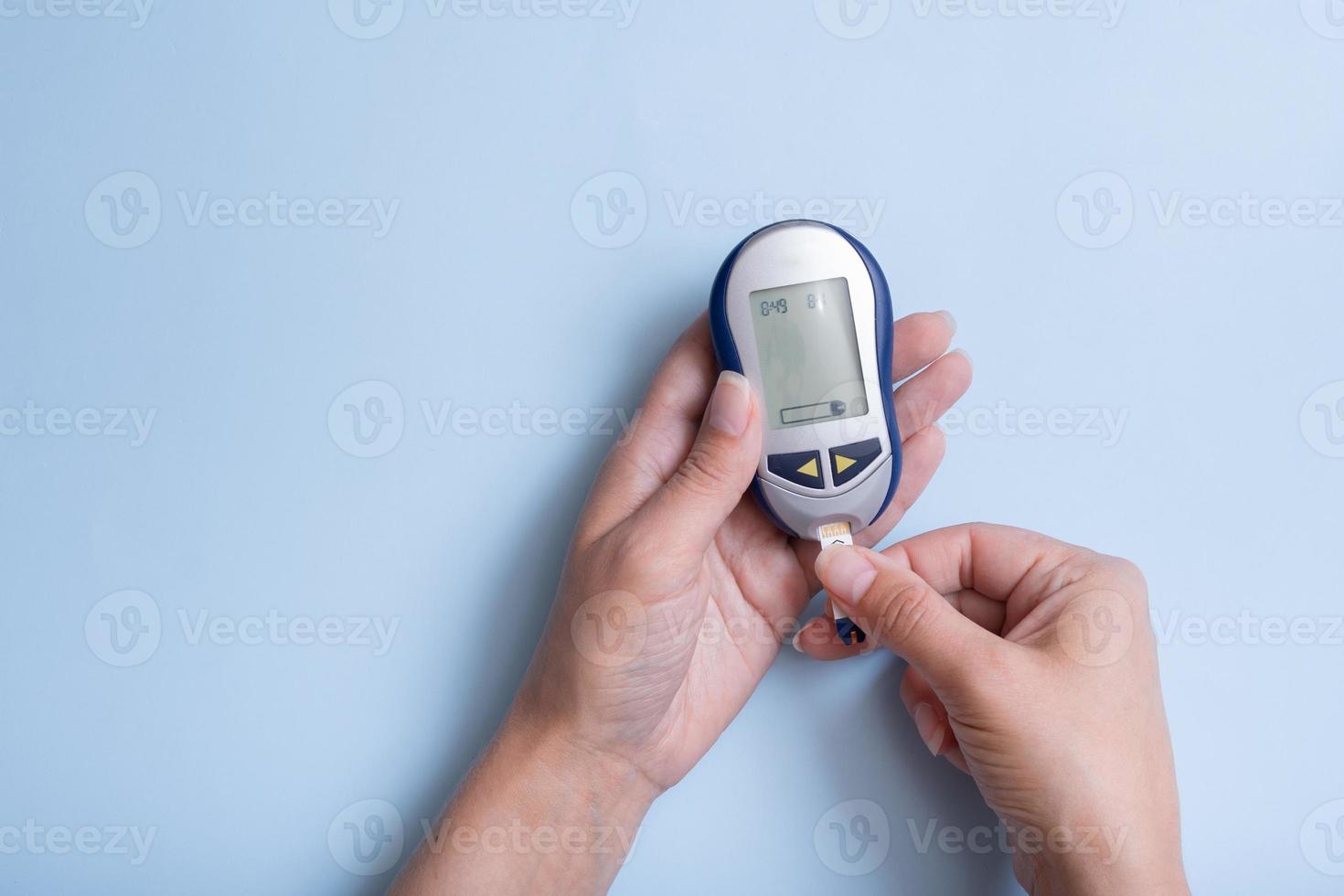vista superior de manos femeninas con medidor de glucosa sobre fondo azul. concepto de diabetes de enfermedad foto