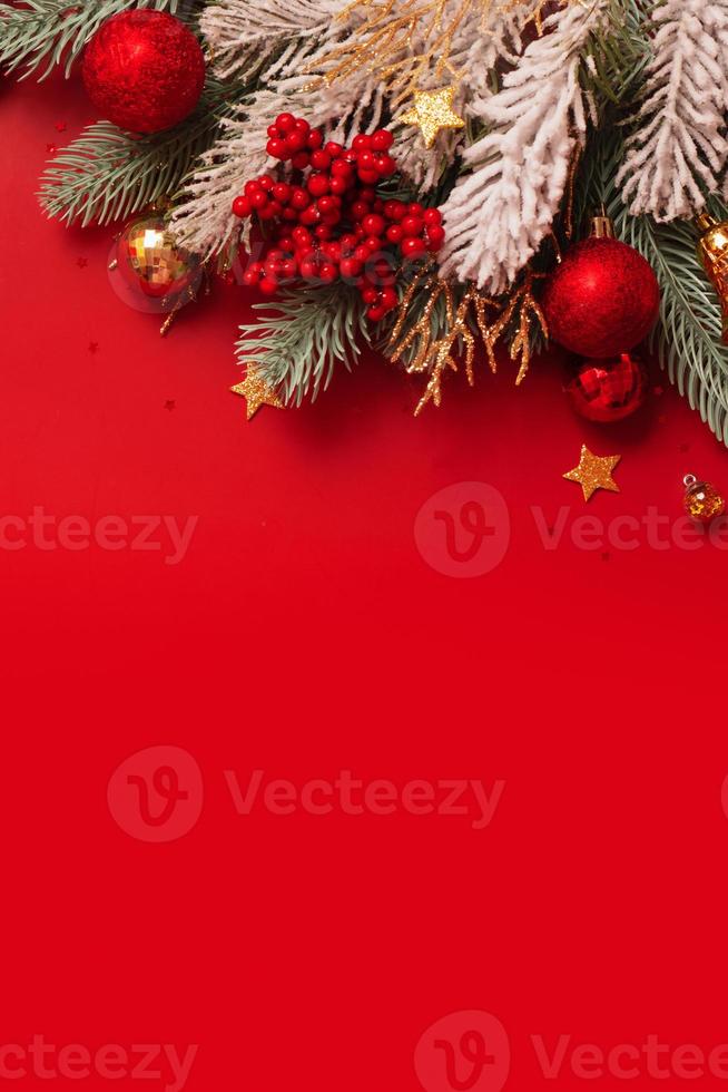 Christmas decoration and pine tree on red background with copy space. New Year greeting card. Flat lay. Vertical format photo