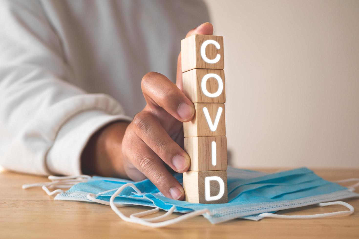 This concept shows campaign for proper mask wearing. Wood blocks with text, COVID. Blue medical mask on table. Disease protection such as influenza, flu, Covid, dust, pm2.5. photo