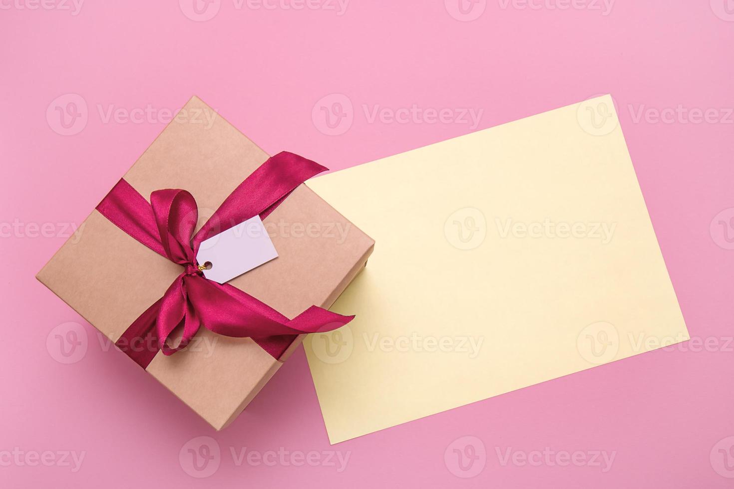 gift box with satin bow and empty tag on pink background with copy space photo