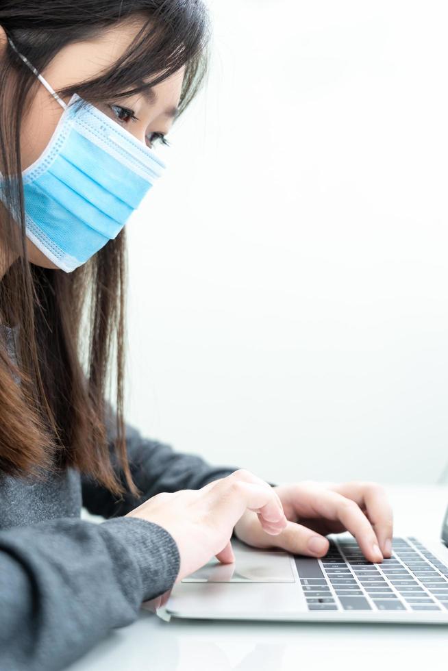 Woman using laptop on desk at home with wearing mask for protect Covid-19 photo