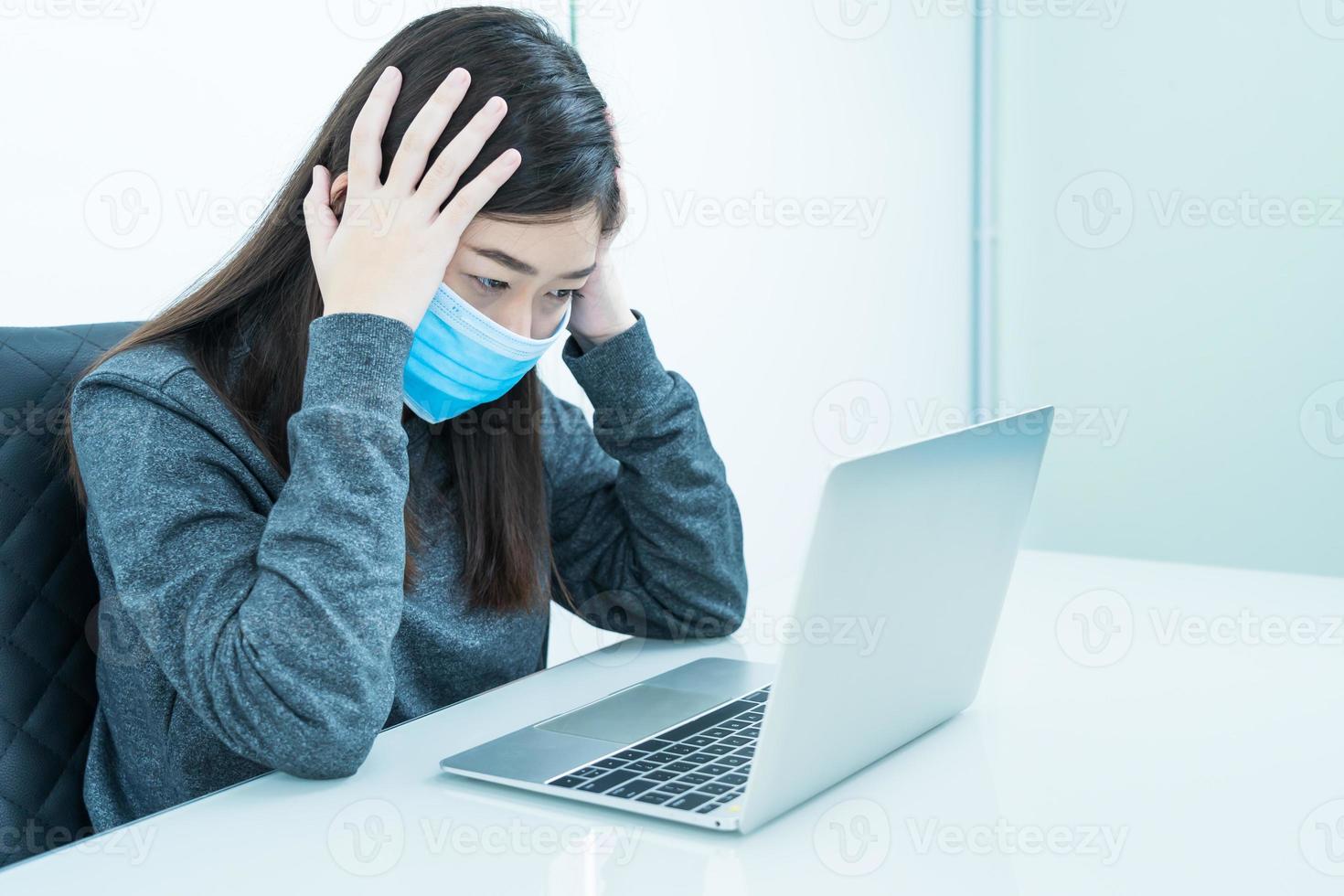 Woman using laptop on desk with headache wearing mask for protect Covid-19 photo