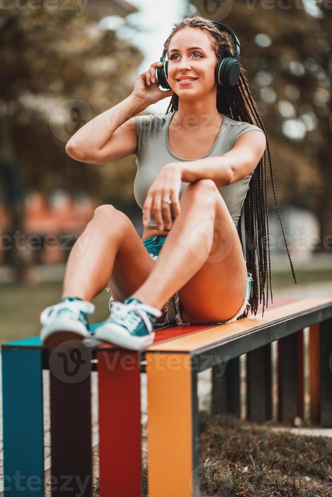 Woman With Long Afro Braids Listening Music On The Bench In The Park photo