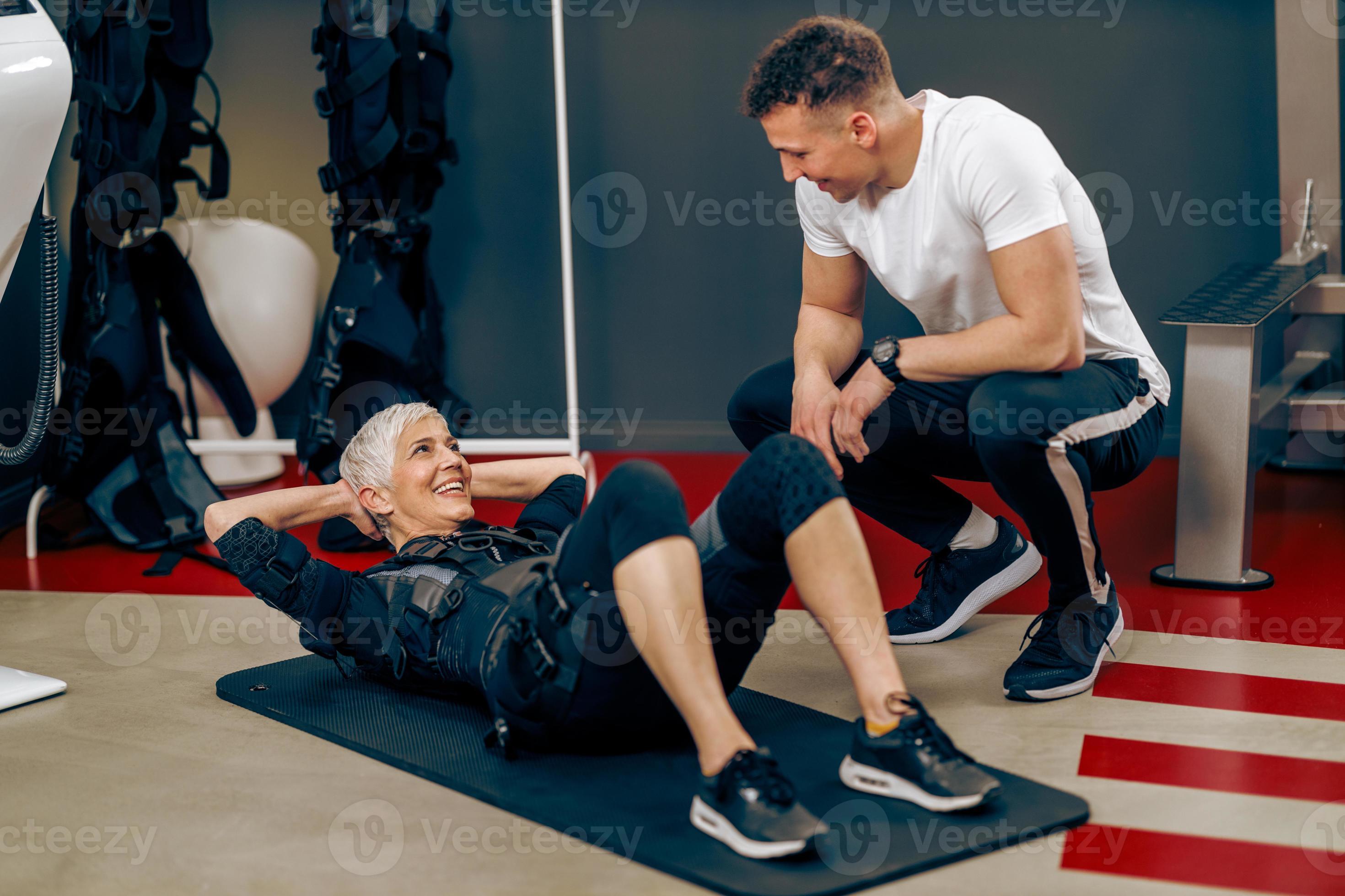 Senior Woman Doing Crunches Exercise During EMS Workout With Coach In