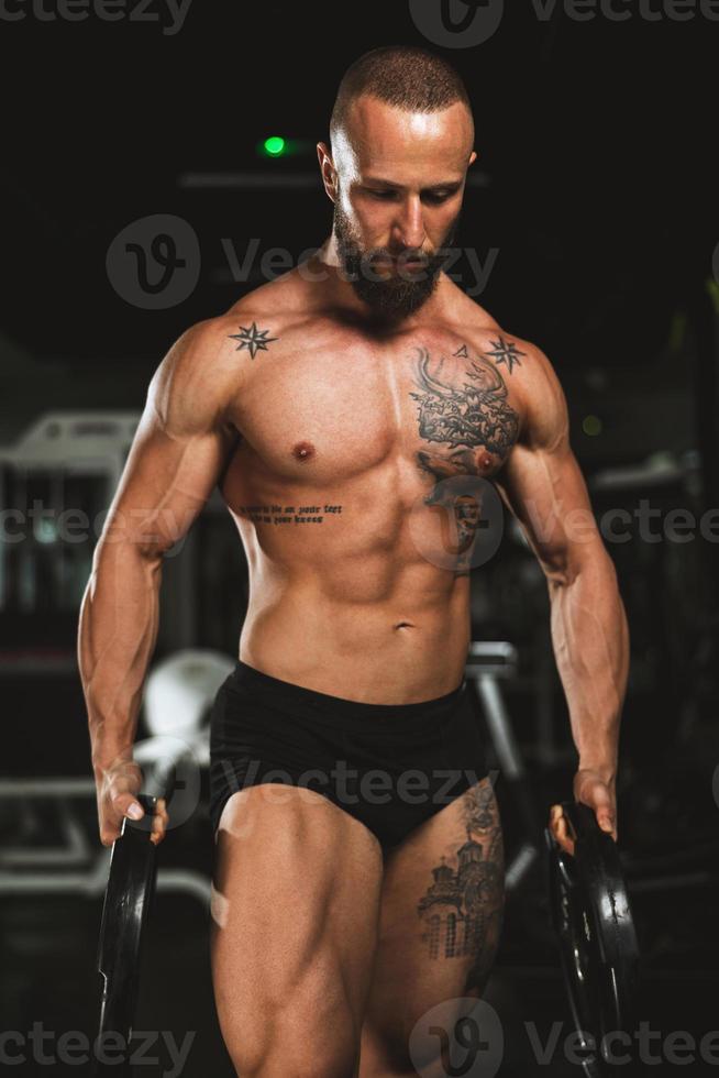 el hombre hace ejercicio con pesas y muestra sus músculos en el gimnasio foto