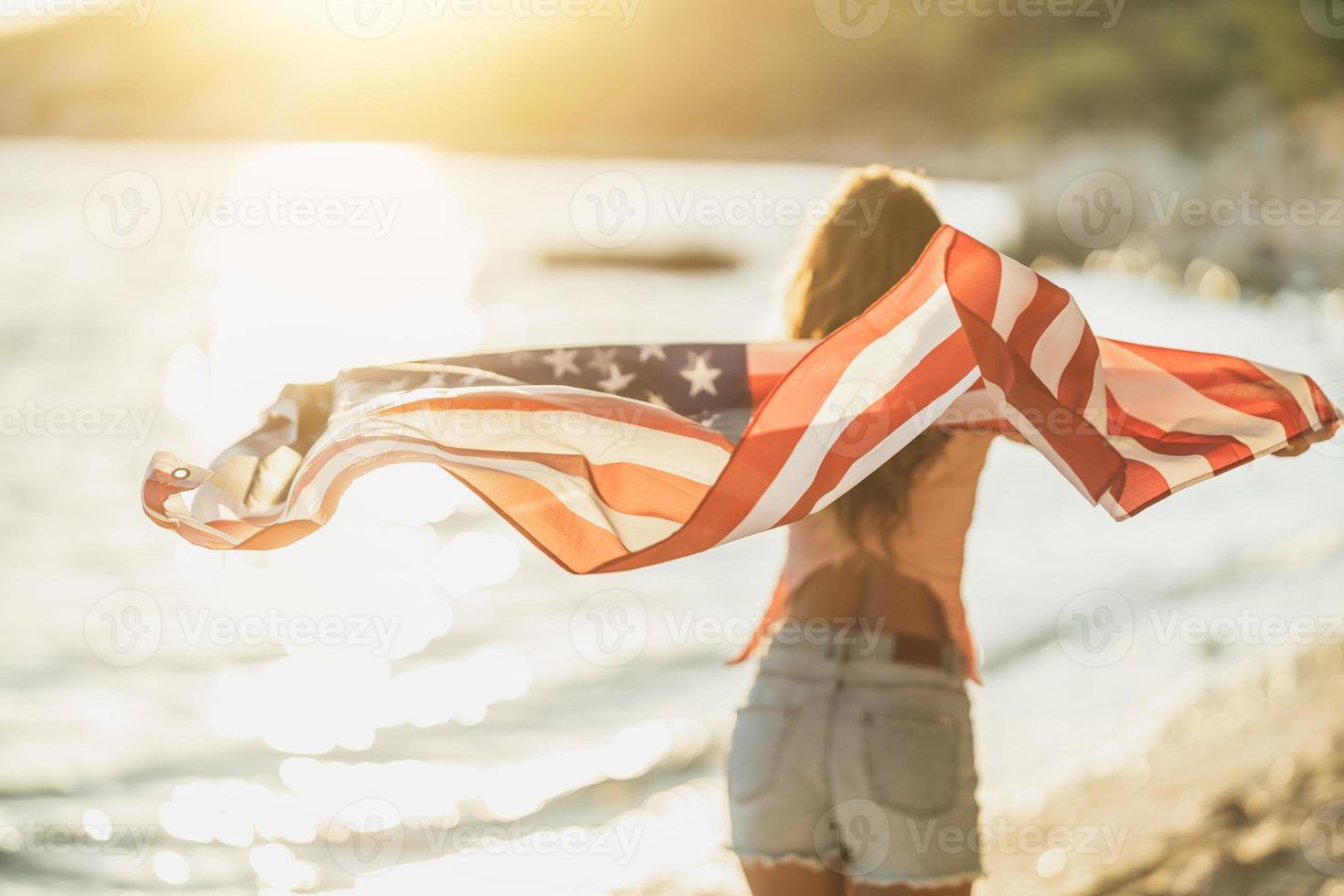 mujer con bandera nacional americana pasando el día en la playa foto