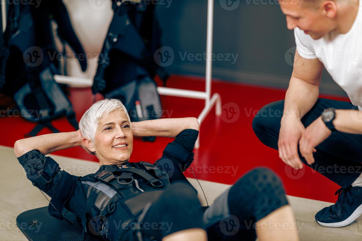 Senior Woman Doing Crunches Exercise During EMS Workout With Coach In The Gym photo
