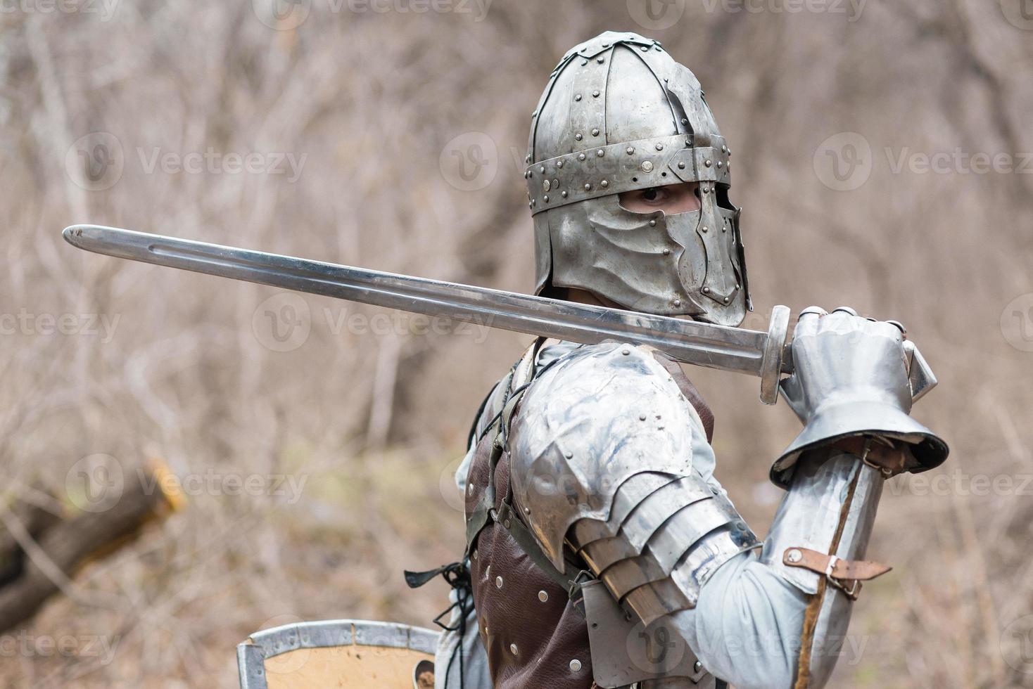 noble guerrero. retrato de un guerrero medieval o caballero con armadura y casco con escudo y espada posando foto