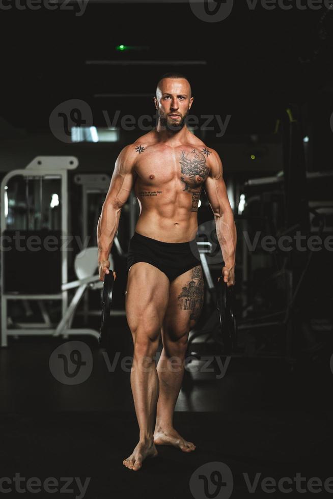 el hombre hace ejercicio con pesas y muestra sus músculos en el gimnasio foto