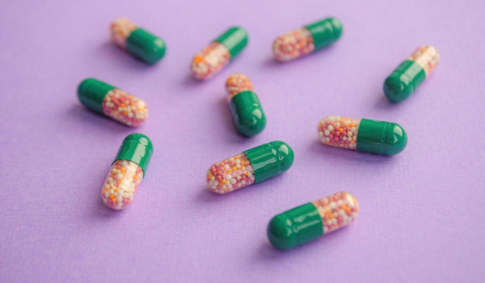 Colored pills. Capsules on a purple background. Transparent colorful pills on a green background. Capsules with granules. Treatment concept. photo