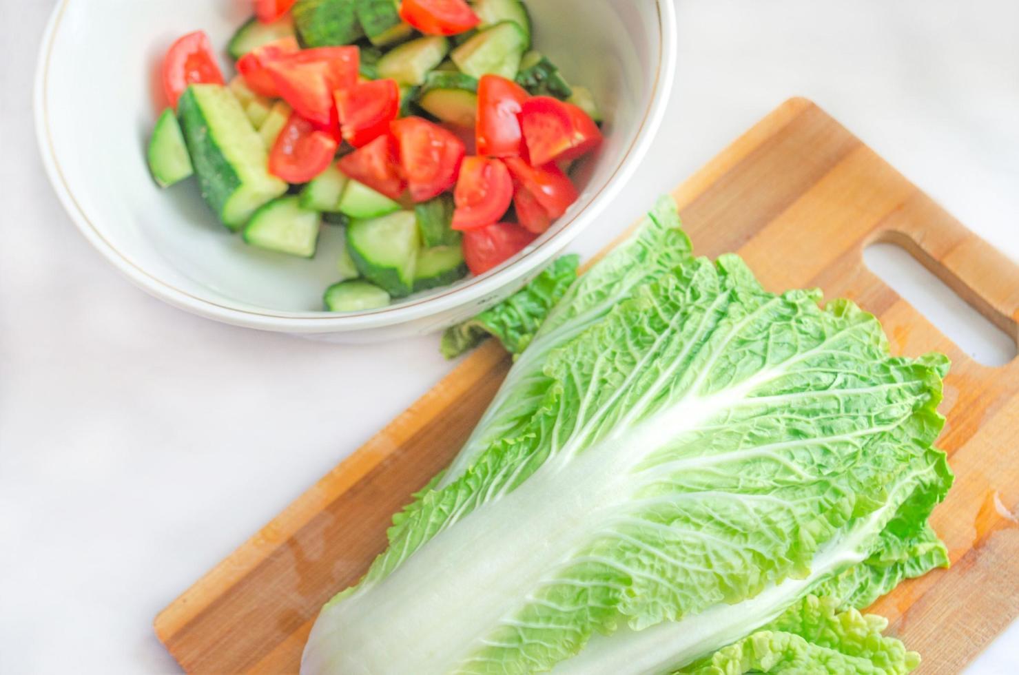 Chinese cabbage and vegetable salad on wooden cutting board. Vegetables on white table. Healthy vegetarian food. Fresh vegetables. Diet concept. Easy vegetarian salad. Cooking a simple salad. photo