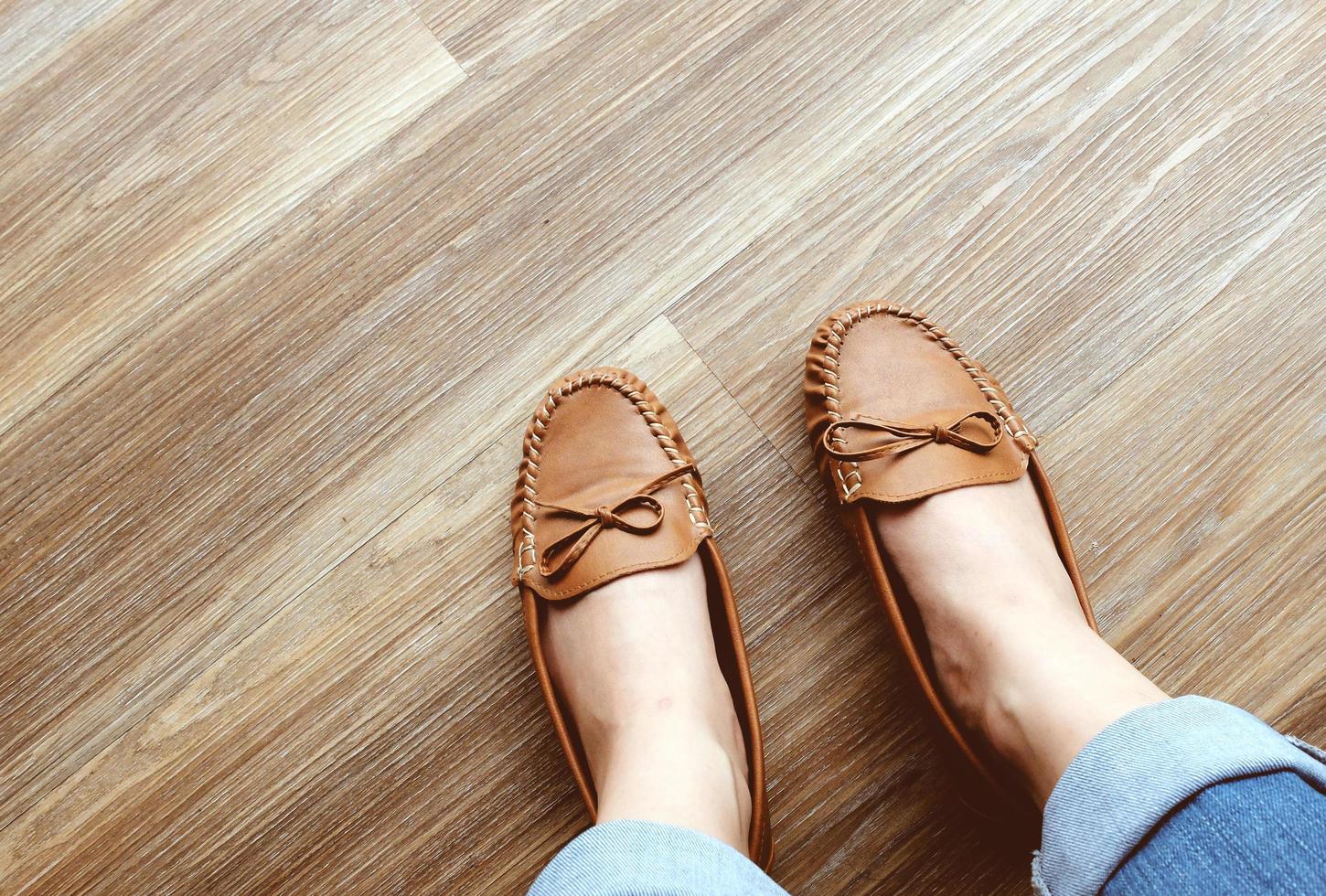 Woman's legs in jeans wearing leather flat shoes on wooden floor photo