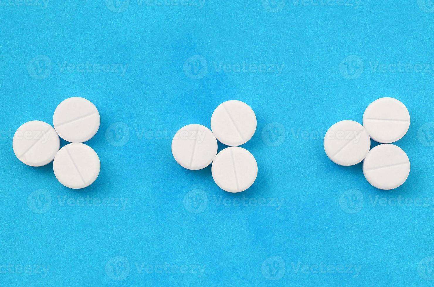 Several white tablets lie on a bright blue background in the form of three triangular arrows. Background image on medicine and pharmaceutical topics photo