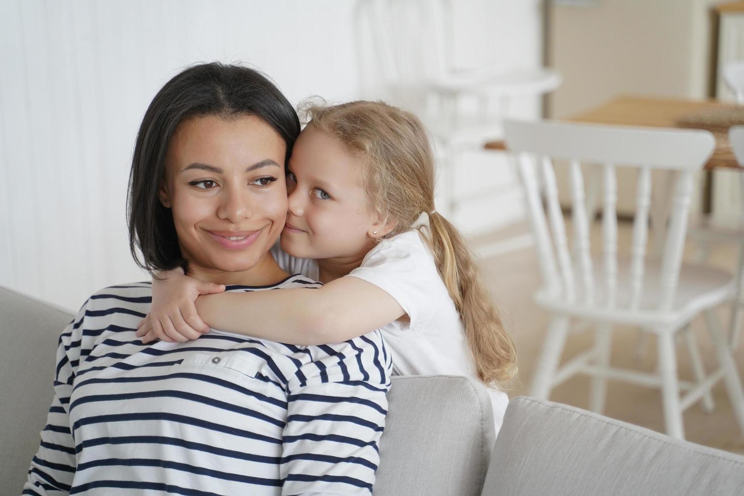 pequeña hija preescolar abrazando a la madre adoptiva, mostrando amor, disfrutando de abrazos juntos en casa foto