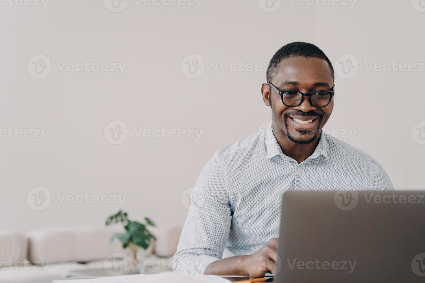 Smiling african american man software developer working online at laptop reads email with good news photo