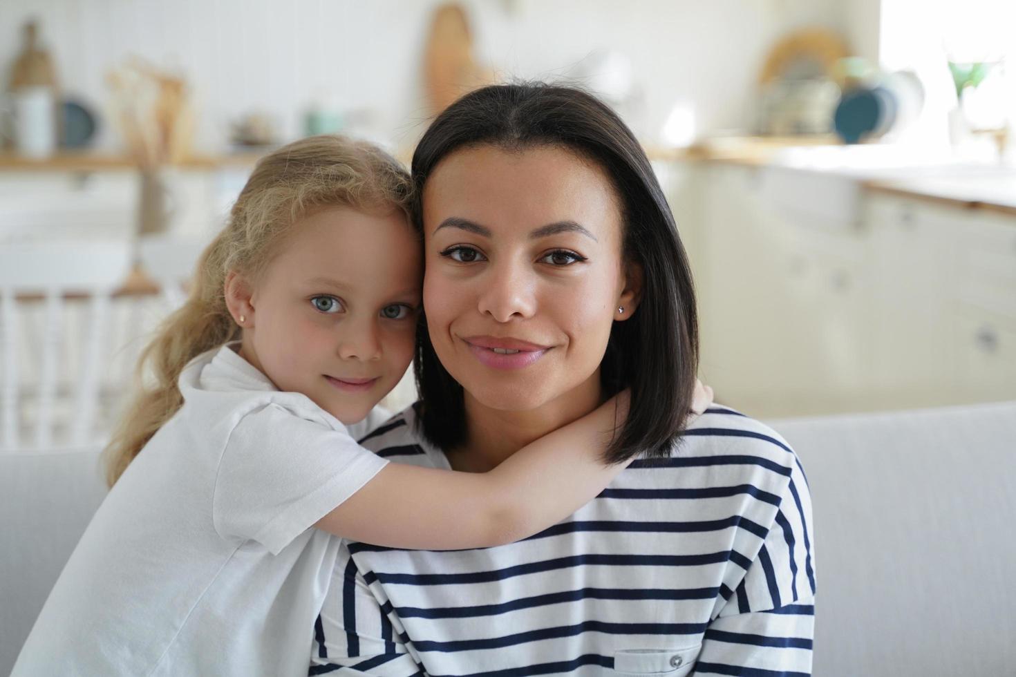 Little adopted daughter hugging foster mother, sitting on sofa at home. Happy motherhood, adoption photo