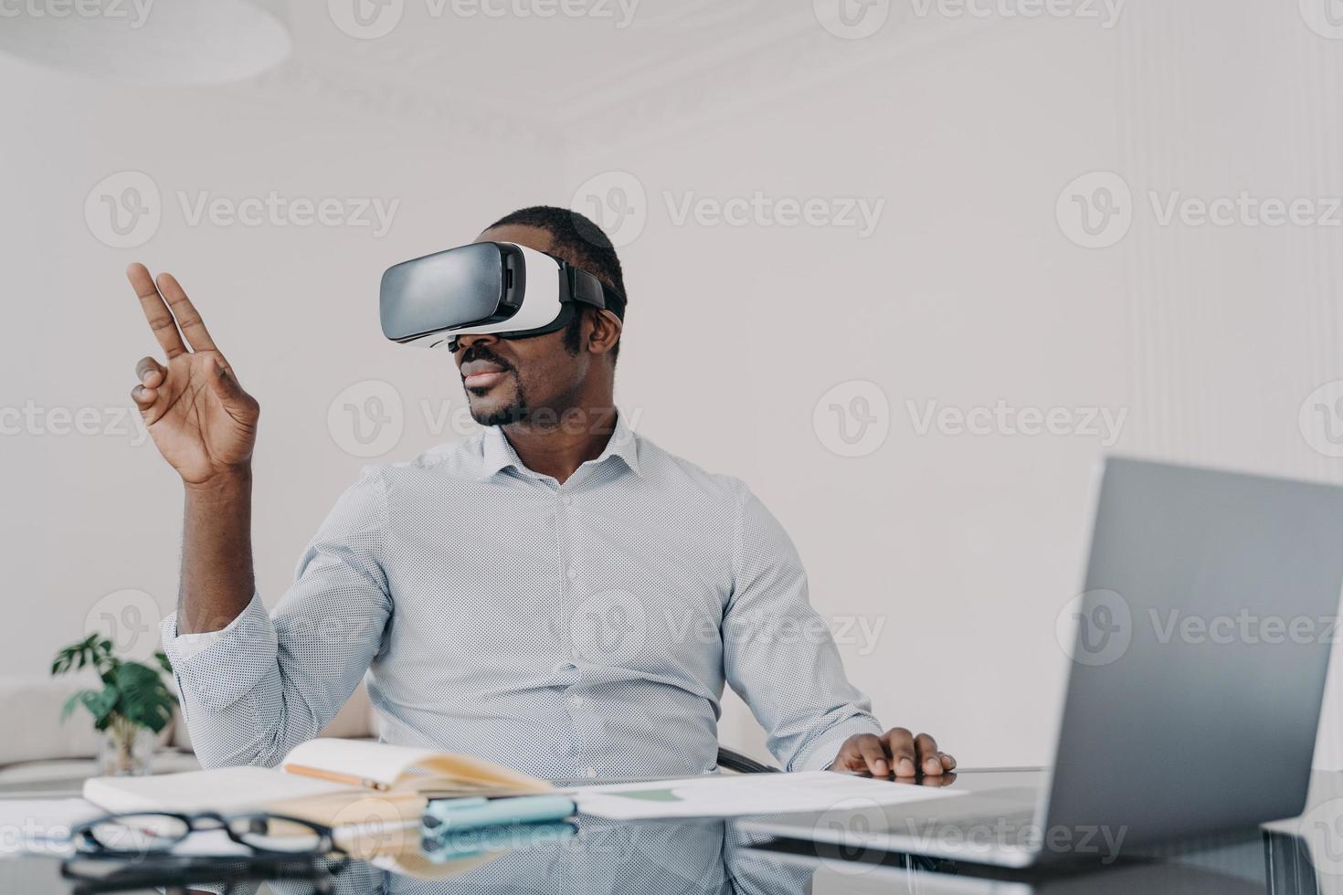 African american businessman in vr glasses working on business project in virtual reality at laptop photo