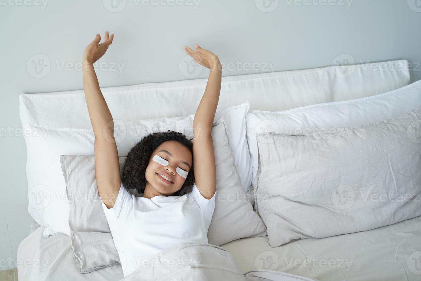 Pretty young girl stretching in cozy bed with under eye patches. Skincare, morning beauty routine photo