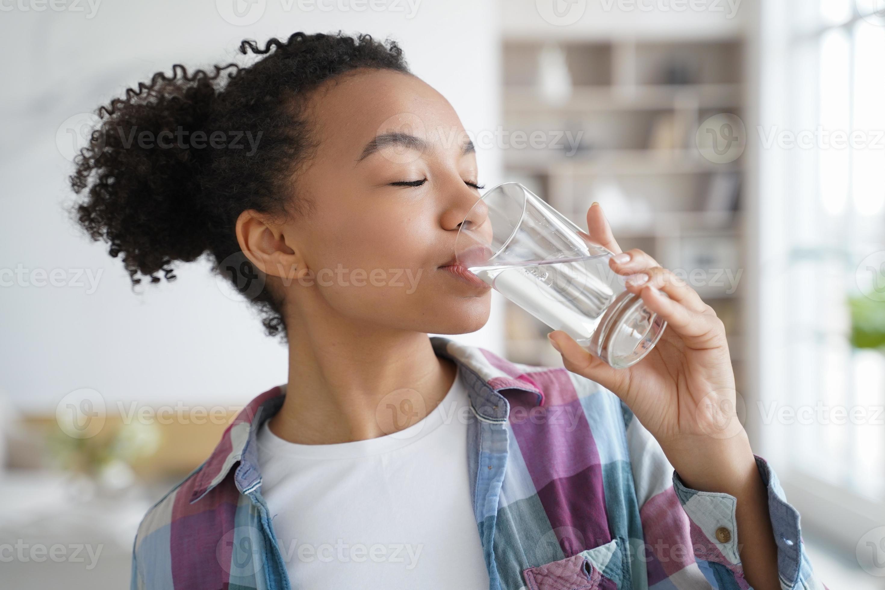 Young mixed race girl drinking clean mineral water at home. Healthy