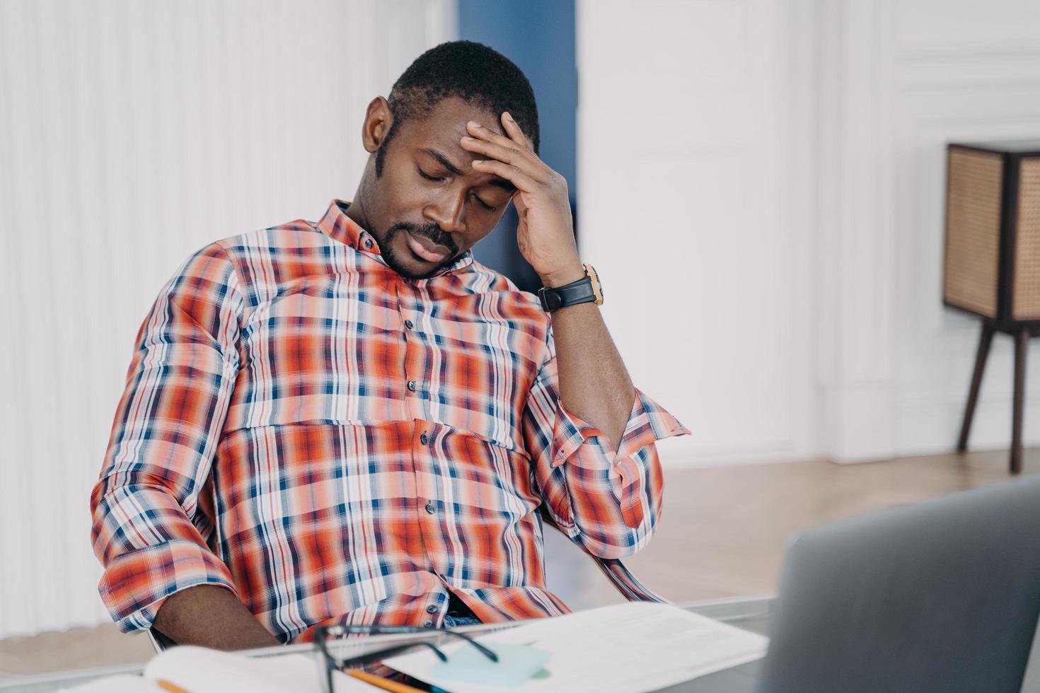 empleado afroamericano cansado que sufre de dolor de cabeza después de trabajar en una laptop. estrés en el trabajo foto
