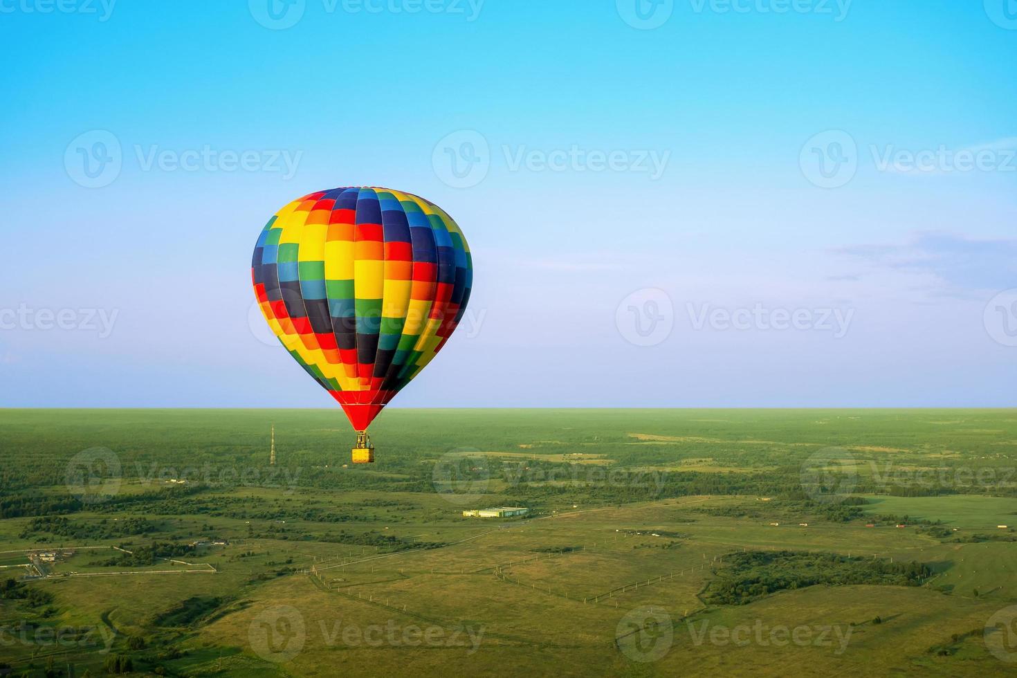 A colorful air balloon is flying in free flight over the field. Bird's-eye view. Multi colored balloon in the blue sky photo