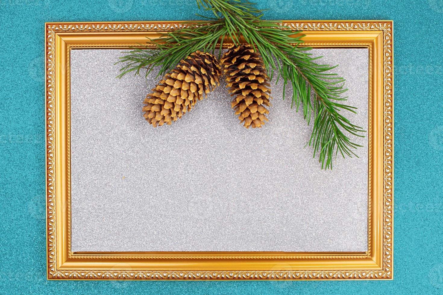 Golden frame with sparkling silver backdrop with spruce branch and cones on blue shiny background. Christmas, New Year. Copy space photo