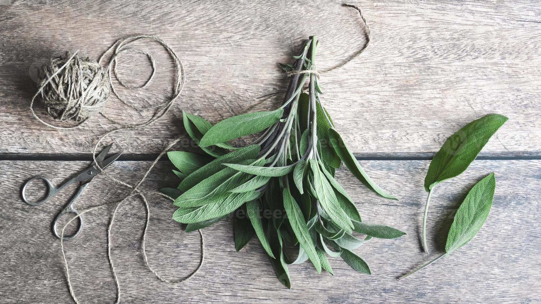 Sage leaves tied with hempstring on wooden table, herbs flat lay, overhead view photo