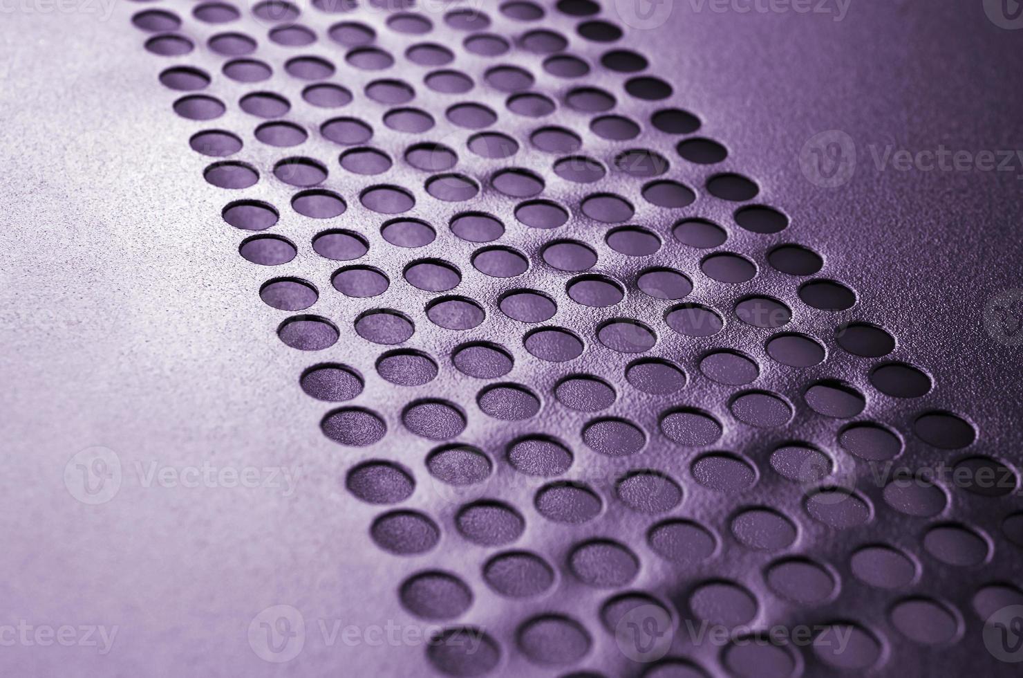 Black metal computer case panel mesh with holes on purple background. Abstract close up photo