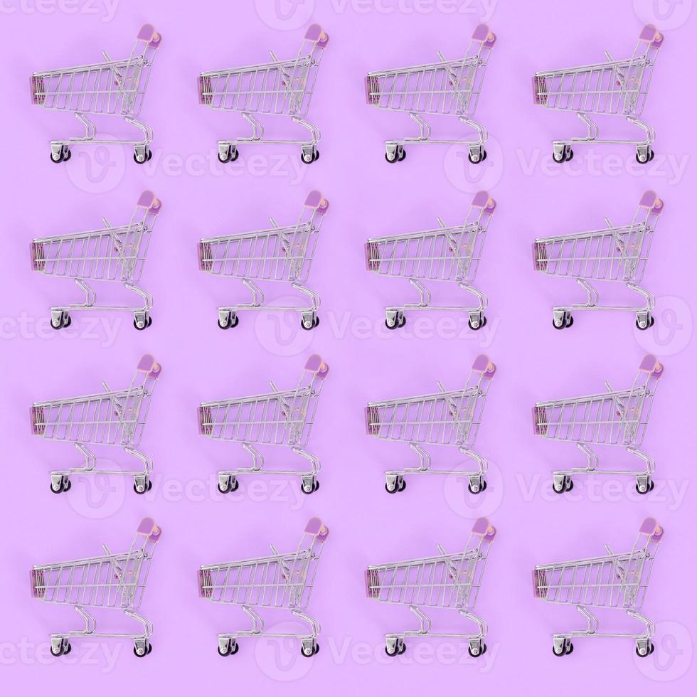 Shopping addiction, shopping lover or shopaholic concept. Many small empty shopping carts perform a pattern on a pastel colored paper background. Flat lay composition, top view photo