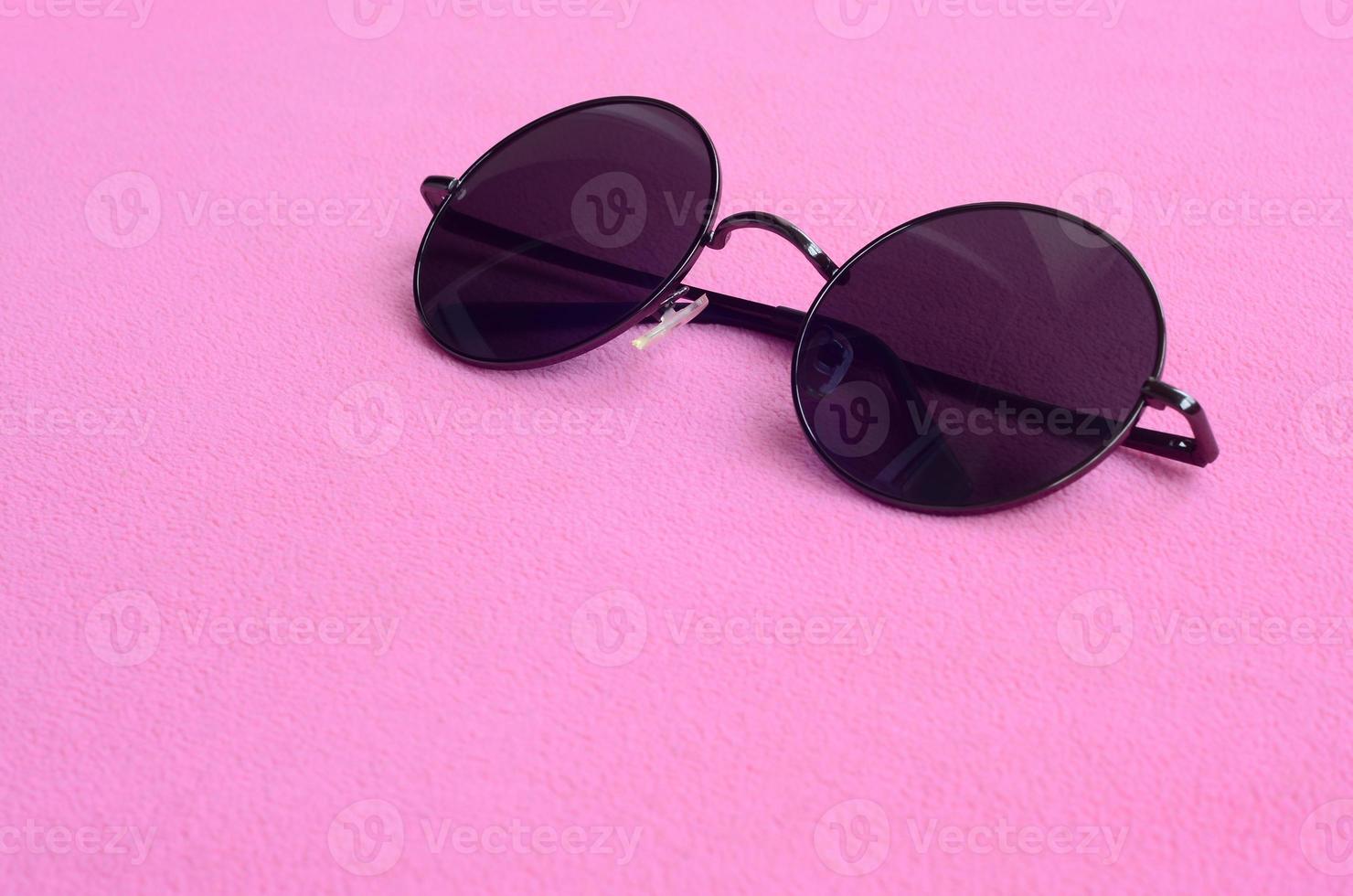 Stylish black sunglasses with round glasses lies on a blanket made of soft and fluffy light pink fleece fabric. Fashionable background picture in female colors photo