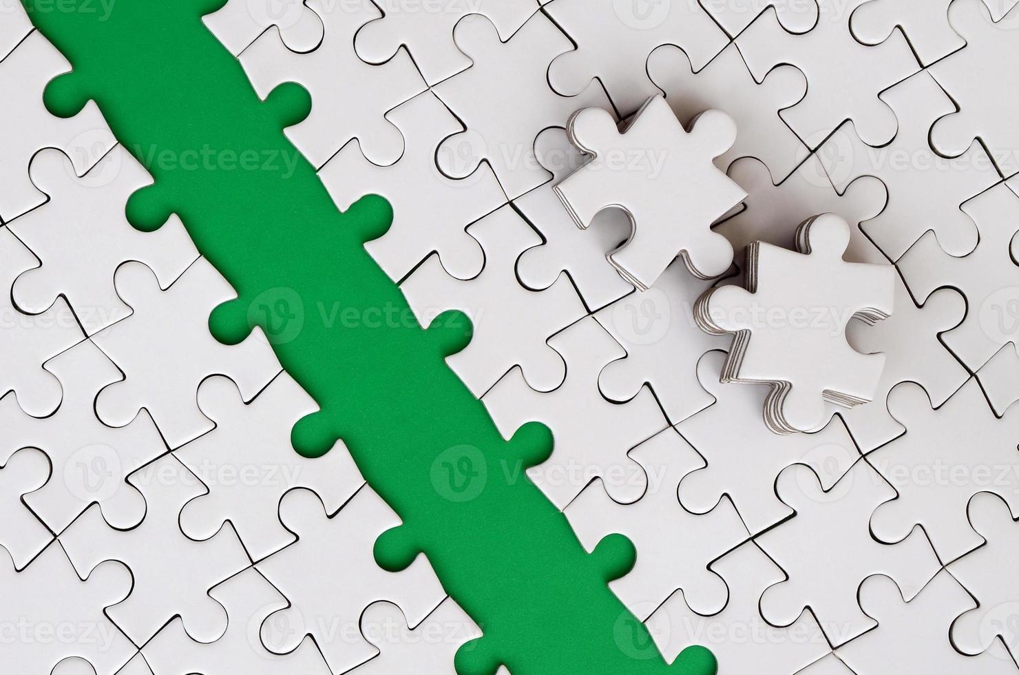 The green path is laid on the platform of a white folded jigsaw puzzle. The missing elements of the puzzle are stacked nearby. Texture image with space for text photo