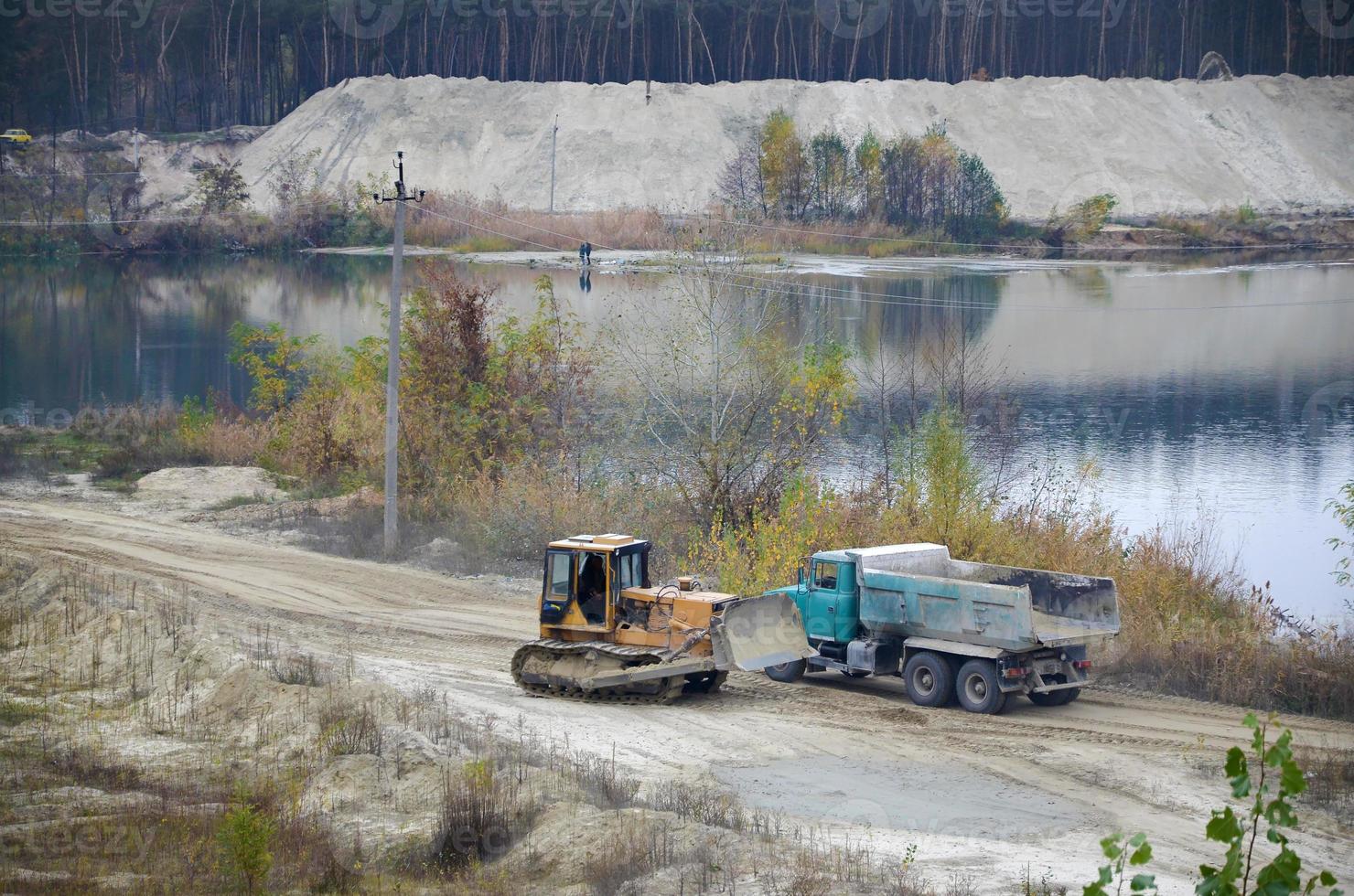 Caterpillar loader and dump truck works at the opencast mining quarry. Heavy machinery in the open pit at river. Dozer and truck on digging operations photo