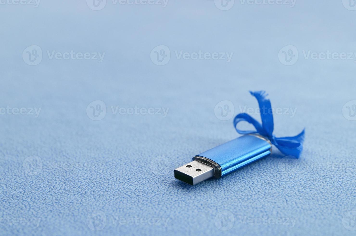 la tarjeta de memoria flash usb azul brillante con un lazo azul se encuentra sobre una manta de tela de vellón azul claro suave y peluda. diseño clásico de regalo femenino para una tarjeta de memoria foto
