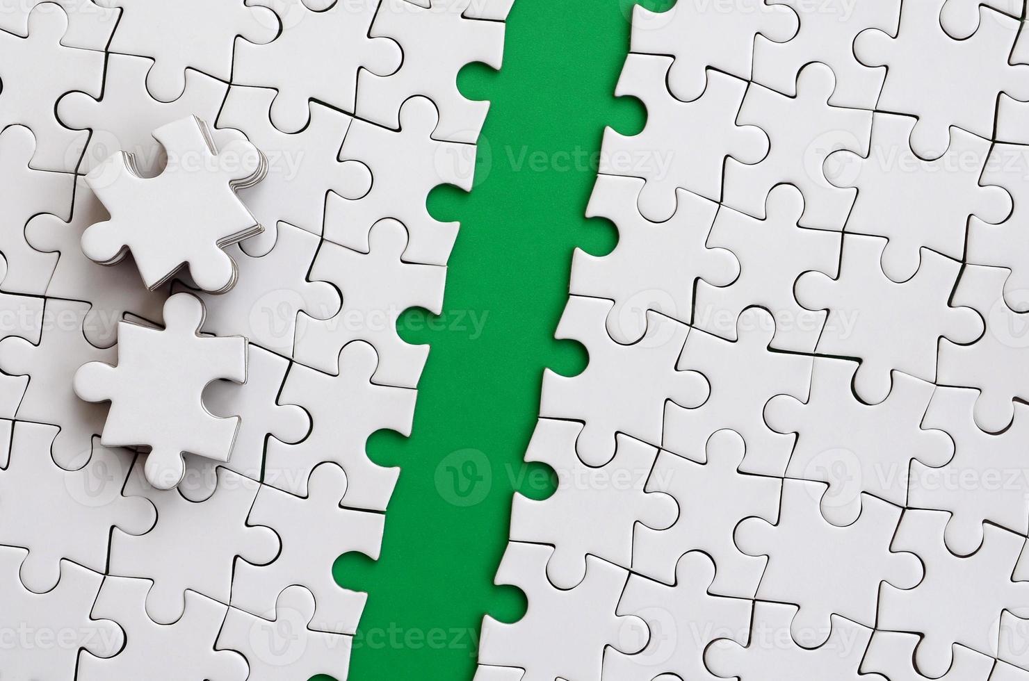 The green path is laid on the platform of a white folded jigsaw puzzle. The missing elements of the puzzle are stacked nearby. Texture image with space for text photo