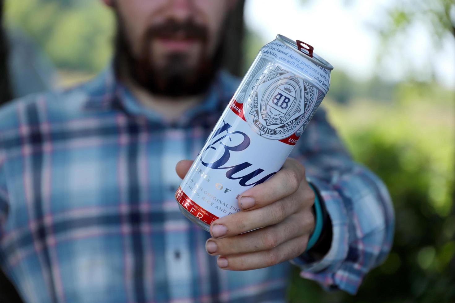 SUMY, UKRAINE - AUGUST 01, 2021 Young man raise Budweiser Bud beer can and shows BUD logo on blurred river and trees background. Budweiser is one of the most popular beer brands in the USA photo