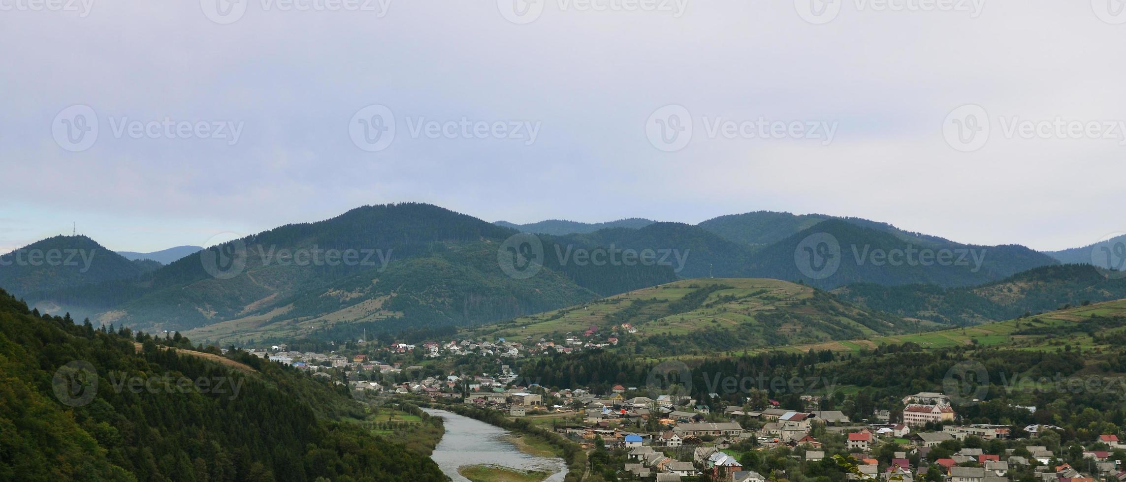 A beautiful view of the village of Mezhgorye, Carpathian region. A lot of residential buildings surrounded by high forest mountains and long river photo