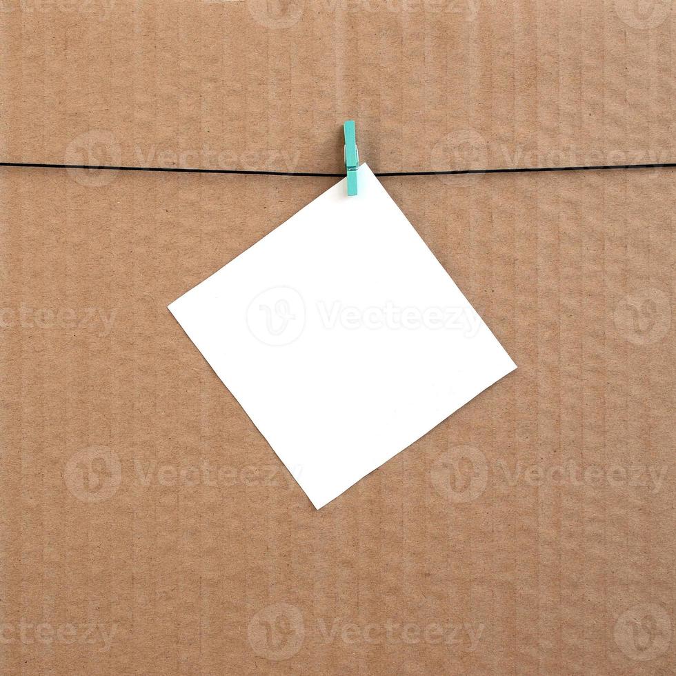 White blank card on rope on a brown cardboard background. Creative reminder, small sheet of paper on wooden clothespin, memo backdrop photo